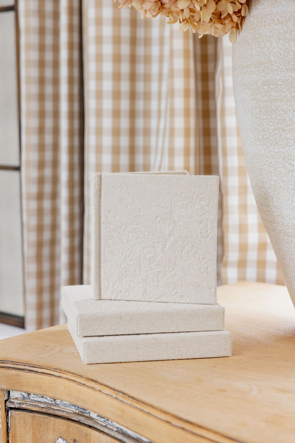 Stack of Little Keepsake Books on a wooden surface with plaid curtains in the background