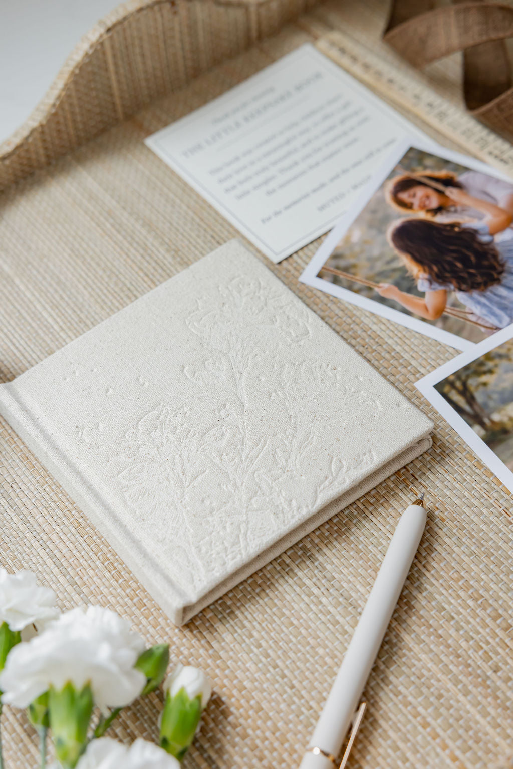 White embossed Little Keepsake Book on a textured surface with photos and flowers