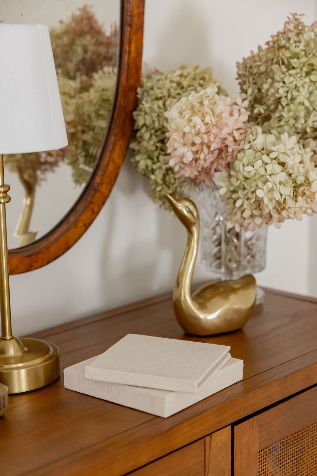 Decorative setup with a gold swan sculpture, lamp, and flowers on a wooden surface.