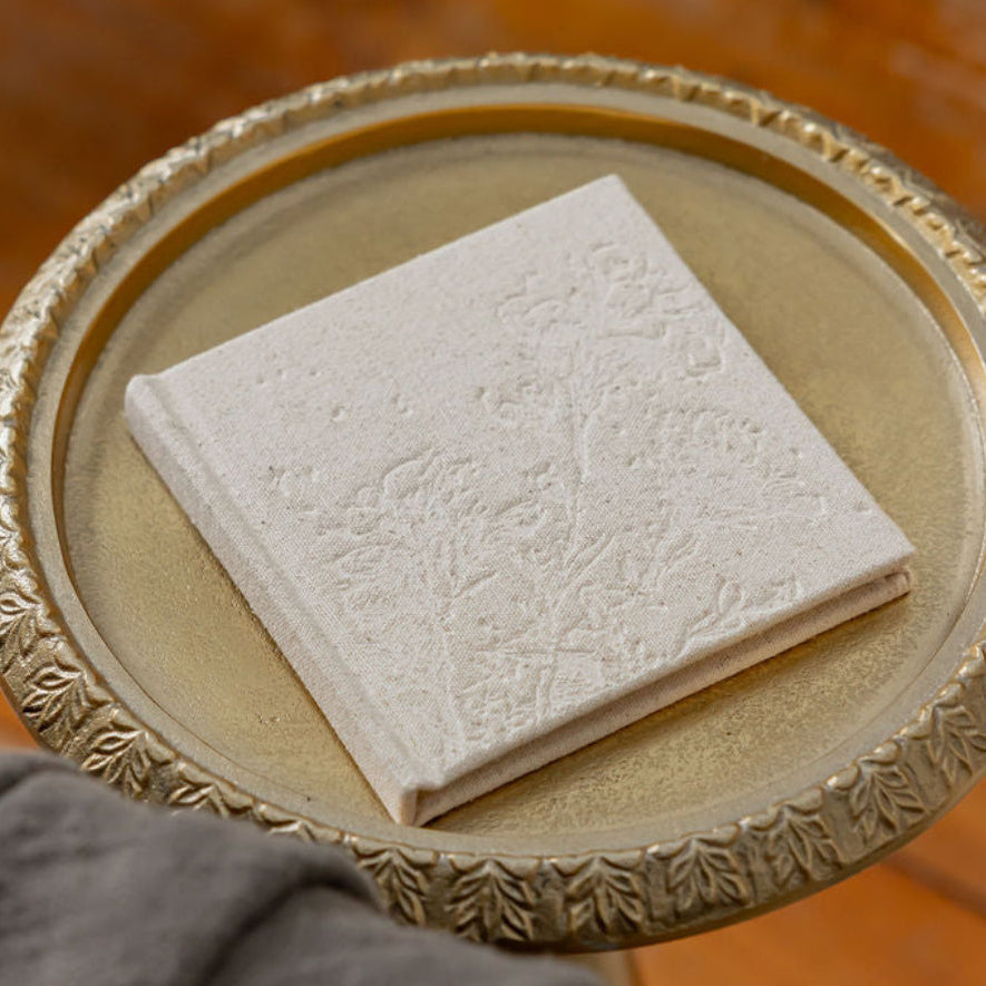 Decorative tray with MUTED + MADE's textured Little Keepsake Book a wooden surface with plants in the background