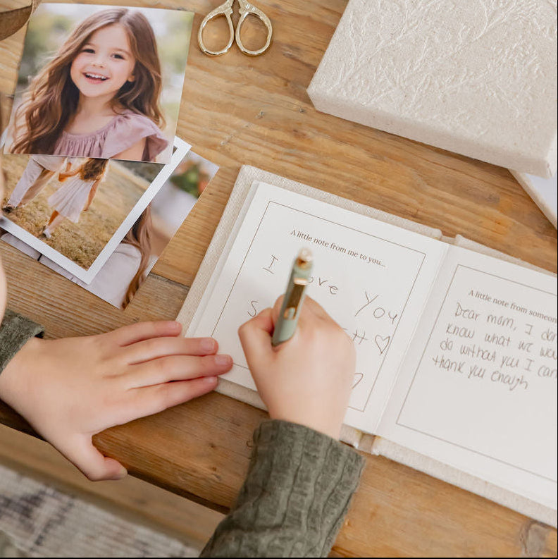 Child writing in a book with a photo of a girl on a wooden table.