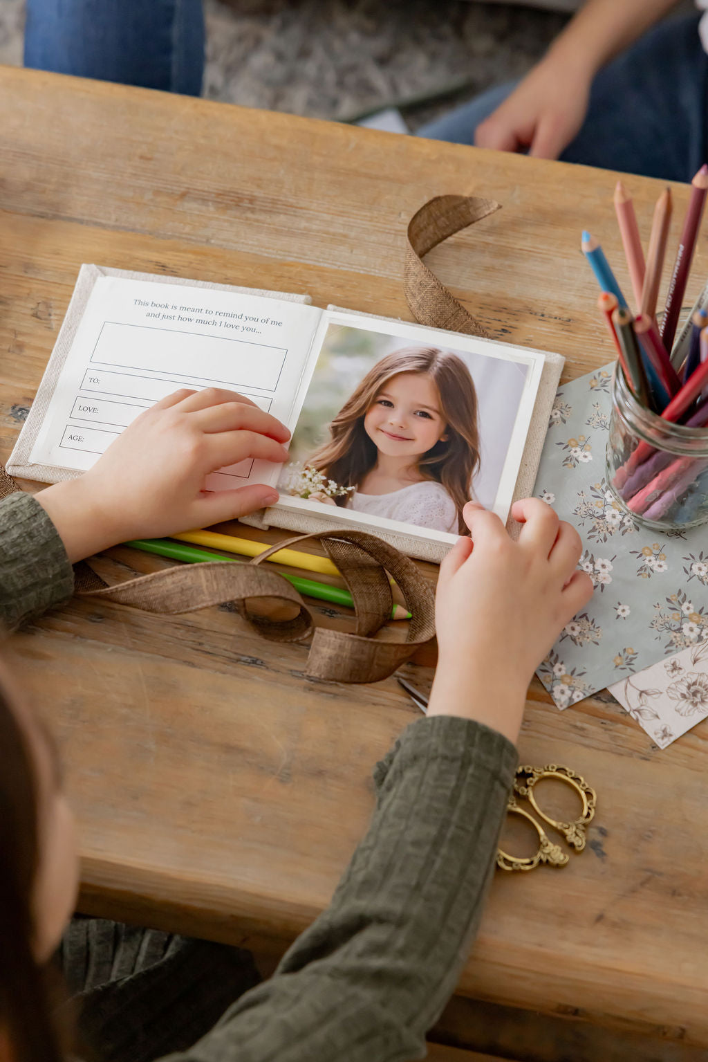 Child's hands holding a photo album with a smiling girl on a wooden table.